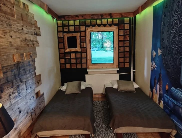 Two twin beds in a narrow bedroom with brick patterned walls and a window overlooking water