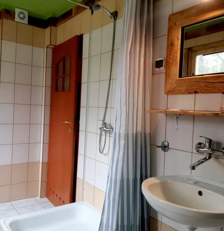 Bathroom with white tile walls, red door, shower curtain, pedestal sink, and wooden framed mirror