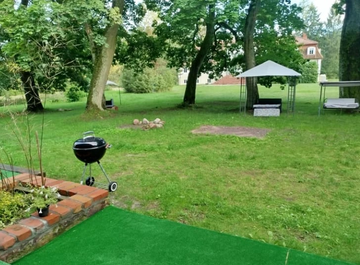 Outdoor park with mini golf course, black ball, wooden ramp, gazebo, shade trees, and grassy field with red brick border