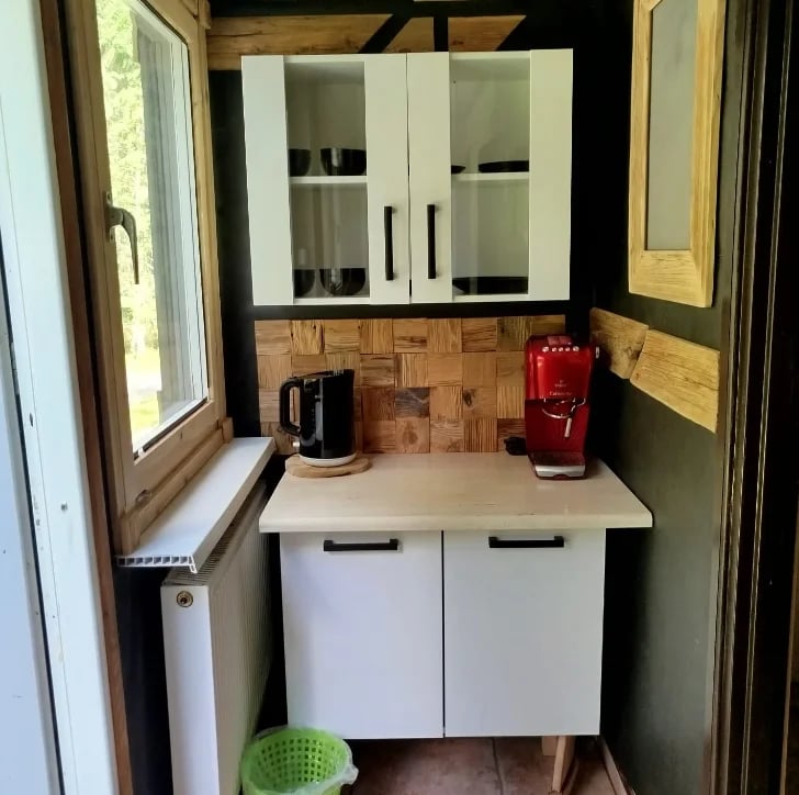 Small kitchen nook with white cabinets, glass-fronted upper cupboards, window, and black kettle and red coffee maker on counter
