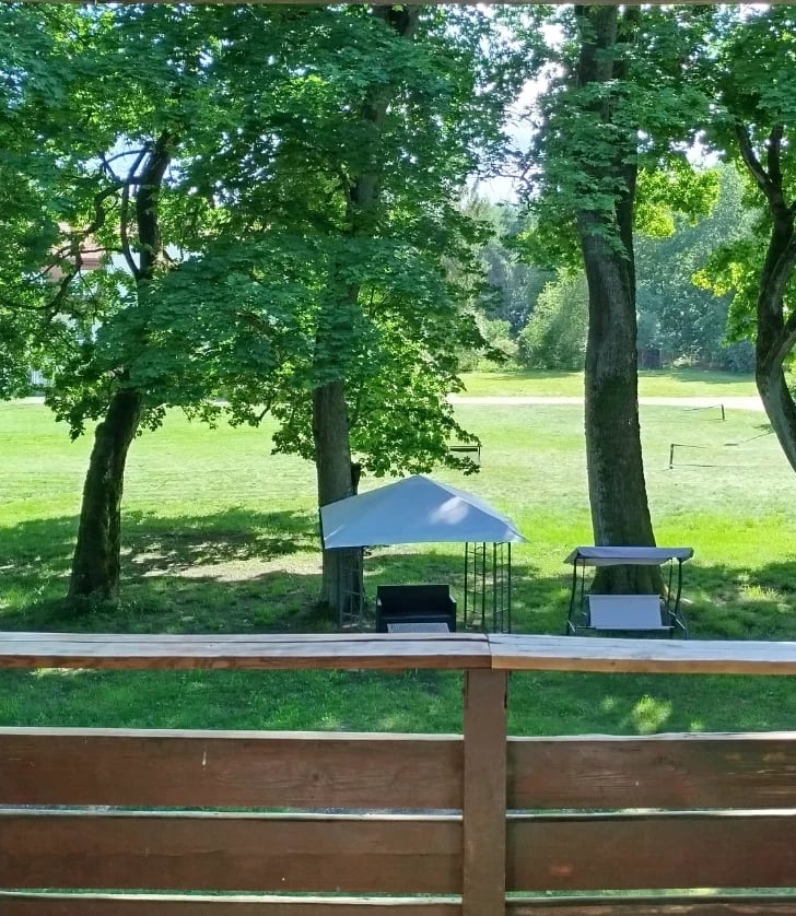 Wooden deck overlooking pastoral landscape with large shade trees, blue canopy, and picnic area