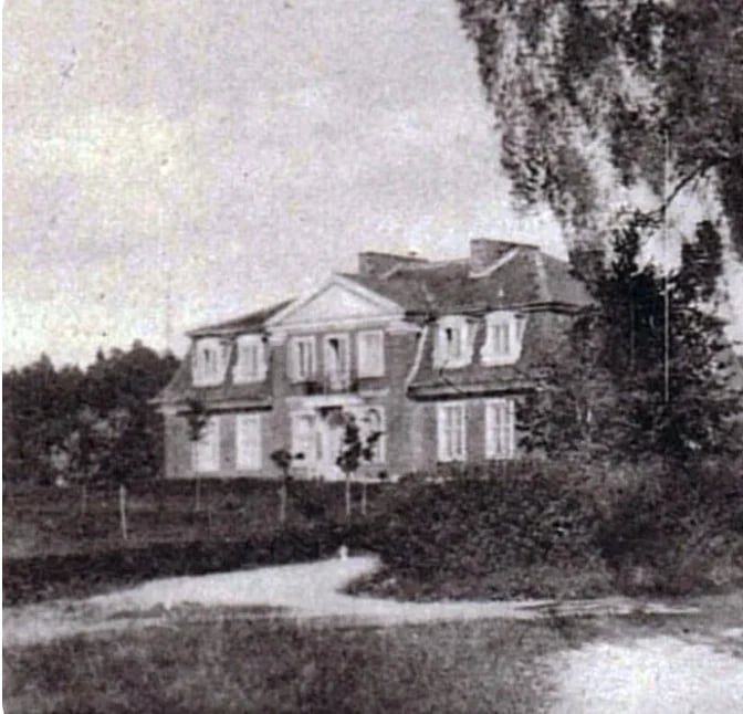 Black and white photograph of a large two-story mansion with shuttered windows, surrounded by overgrown vegetation and trees