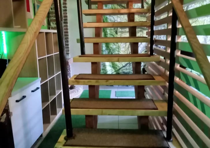 Wooden staircase with black metal railings and handrails viewed from below, showing steps leading upward in an indoor setting