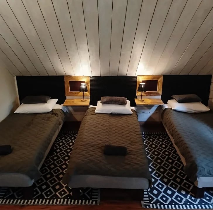 Modern bedroom with three beds arranged side-by-side, wooden headboards with reading lights, white ceilings, and patterned carpet flooring