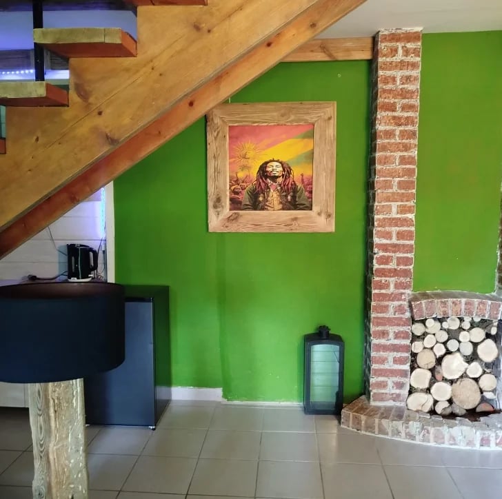 Interior room with bright green wall, framed religious portrait, wooden beam ceiling, brick fireplace with firewood, and modern furniture