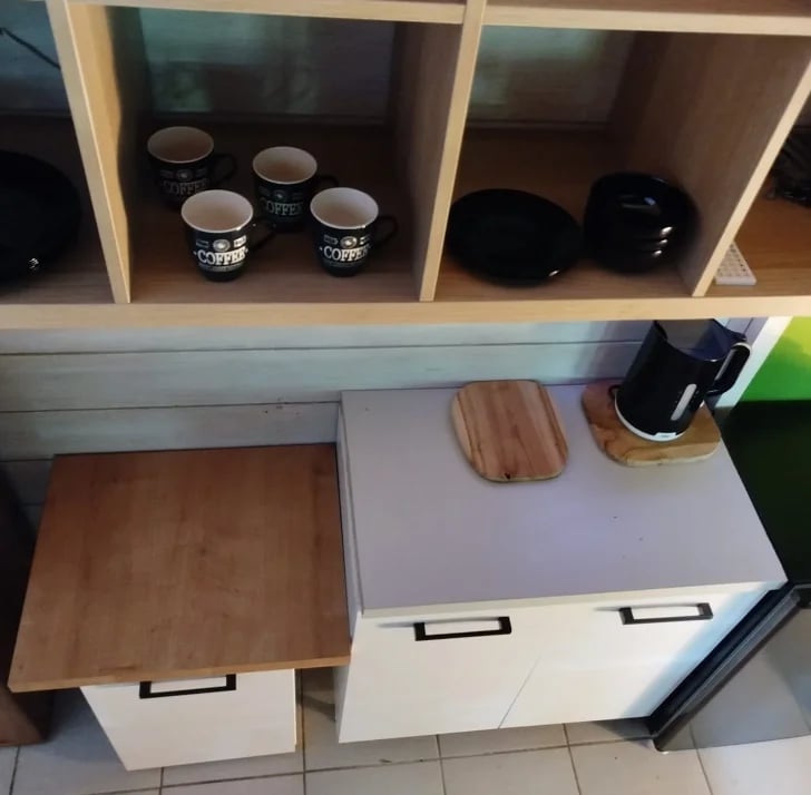 Modern kitchen counter with white cabinets, wooden countertop section, black appliances, and shelving unit displaying bowls and kitchen items