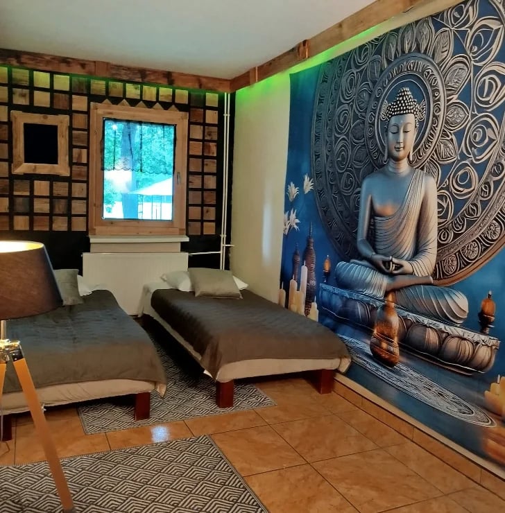 Modern bedroom with Asian-inspired decor, featuring two dark beds, a large Buddha wall mural, geometric patterned wall, and natural light from a window