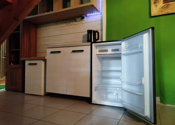 Open refrigerator and white kitchen appliances displayed against a green wall in a showroom setting