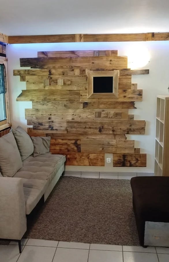 Rustic wood plank accent wall with mounted flat-screen TV, beige sofa and dark armchair in modern living room