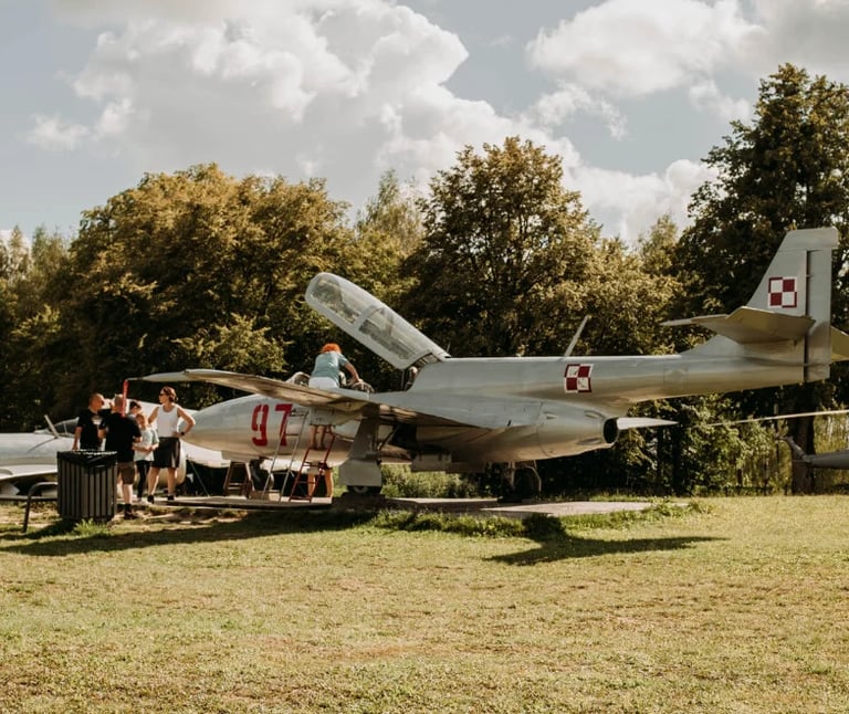 Visitors viewing a vintage military aircraft with open cockpit at an outdoor aviation museum on a grassy field