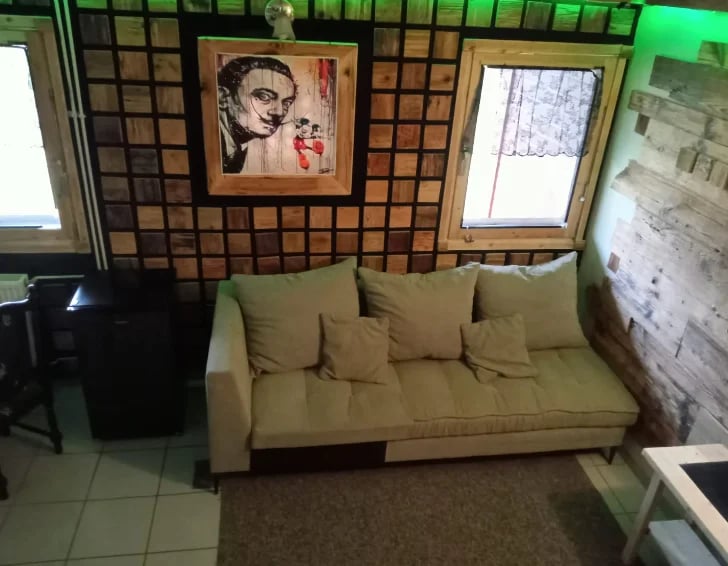 Beige sofa with cushions against a tiled wall with framed artwork and windows in an interior space