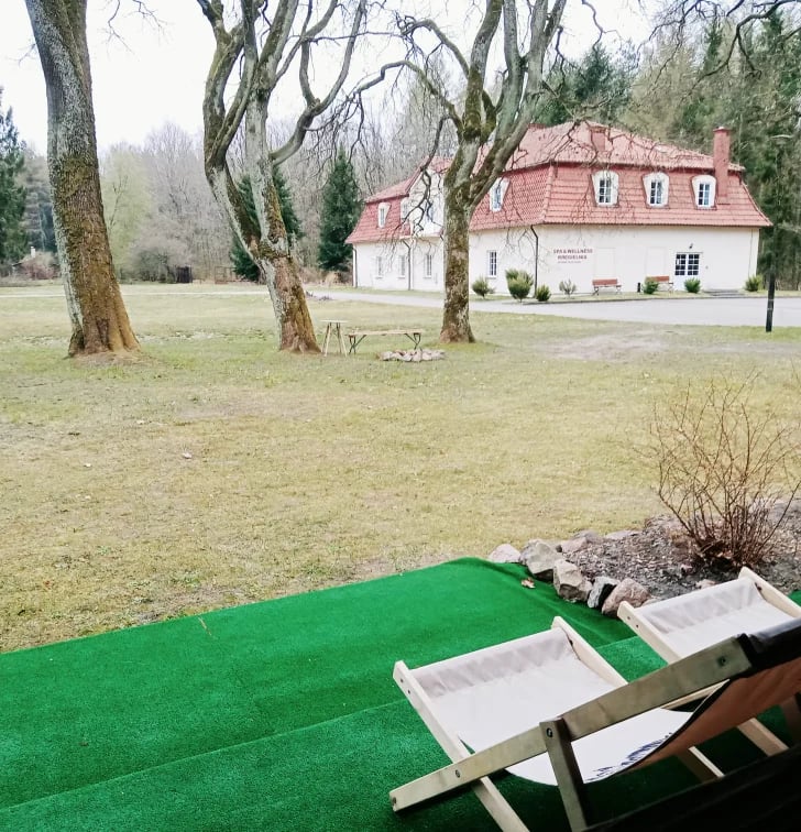 Miniature golf course with white trays on green turf, old trees, and a white cottage with red roof in the background