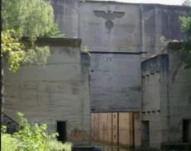Overgrown concrete bunker or fortress with wooden doors, cross on top, and green vegetation surrounding structure