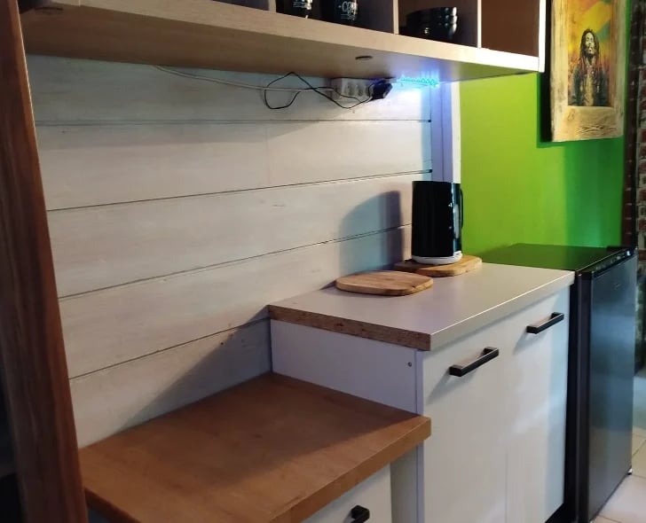 Modern desk workspace with white shelving unit, wood countertop, green accent wall, and integrated lighting