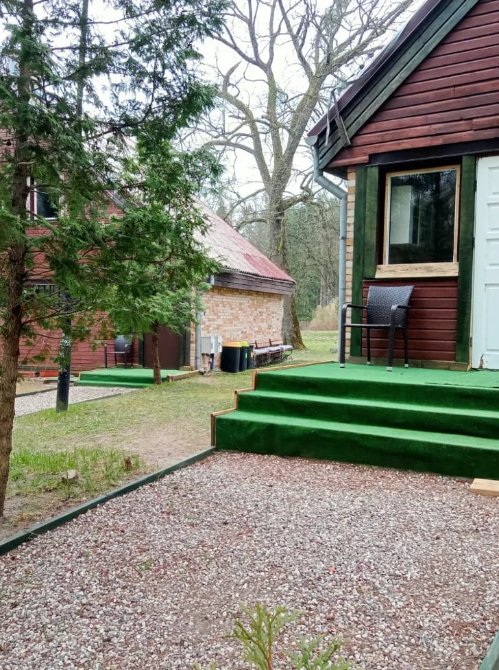 A rural cottage with green trim and a gravel courtyard, surrounded by bare trees and brick buildings