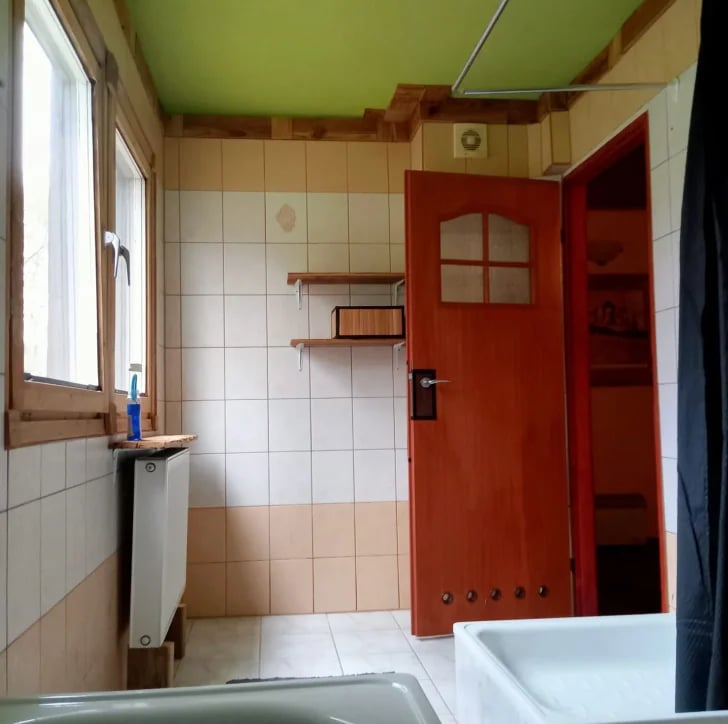 Vintage bathroom with white tile walls, red wooden door, wooden shelves, window with natural light, and bathtub